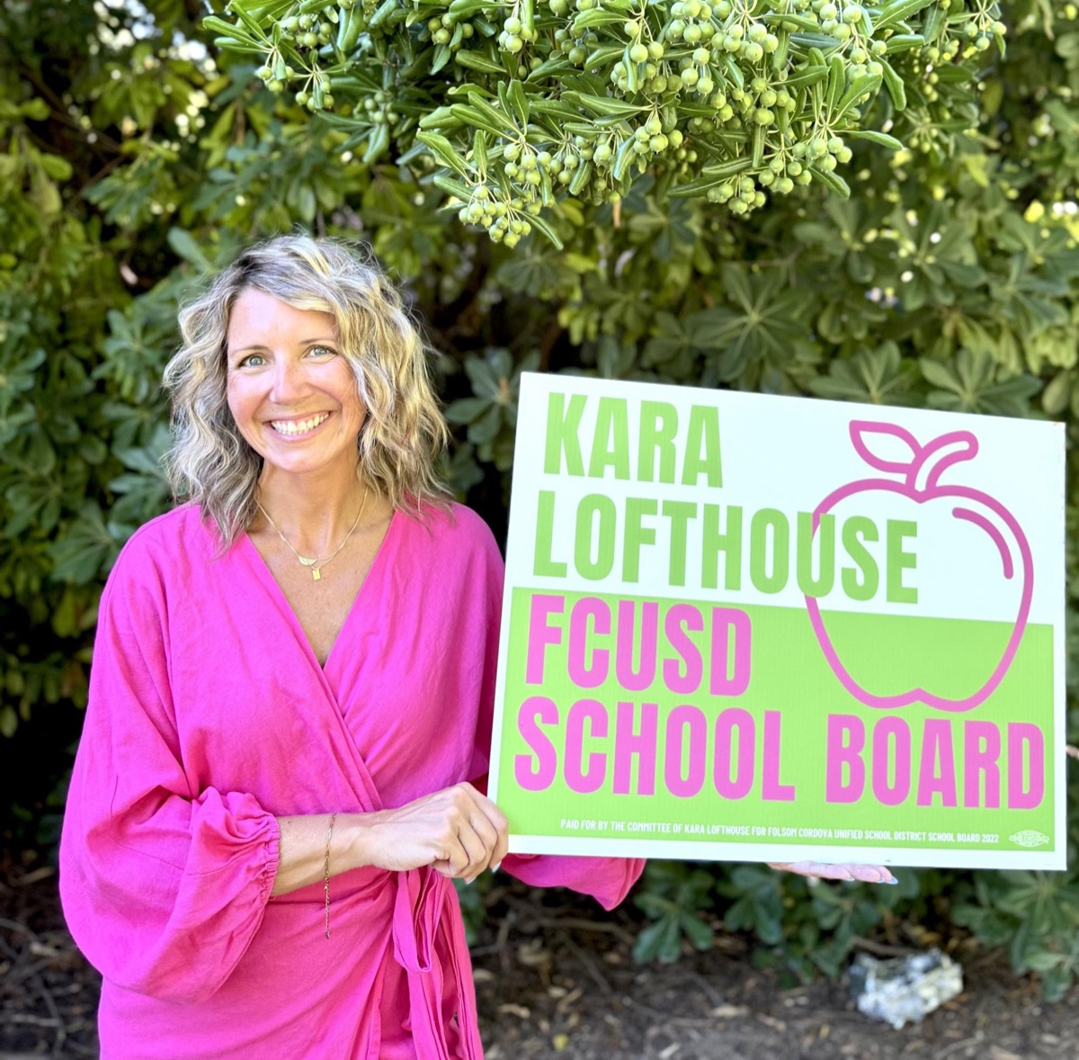 Kara Lofthouse holding her pink and green campaign yard sign